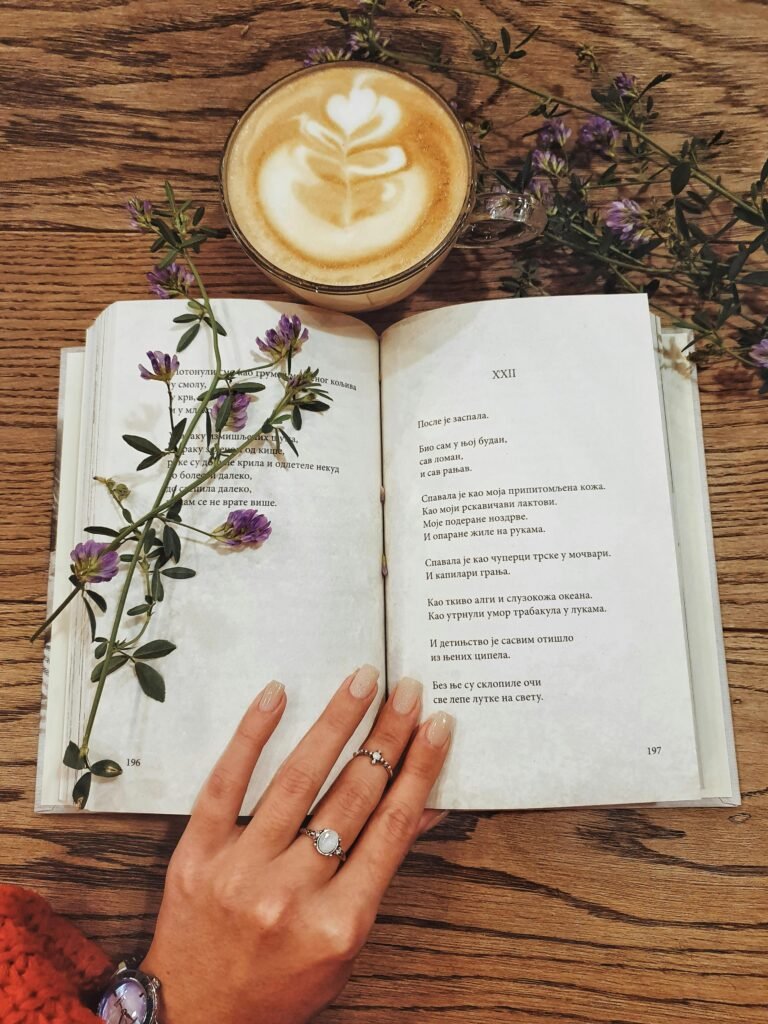 Relax with a latte and poetry on a wooden table adorned with flowers and an open book.